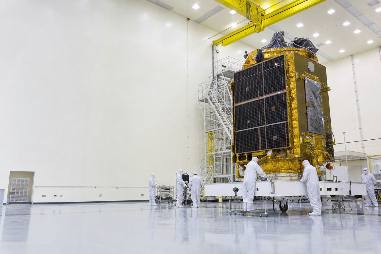 Engineers in white cleanroom suits working around a gold-foil-wrapped satellite inside a spacecraft integration hall.